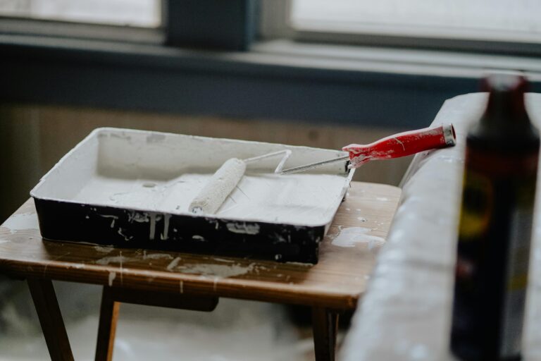 A paint roller and tray with white paint on a wooden table, indicating a renovation work.